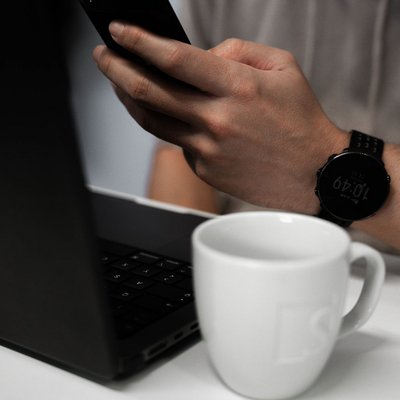 Imagebild mit Person die Smartphone bedient und vor einem Laptop sitzt. Daneben steht eine SIWA Kaffee Tasse